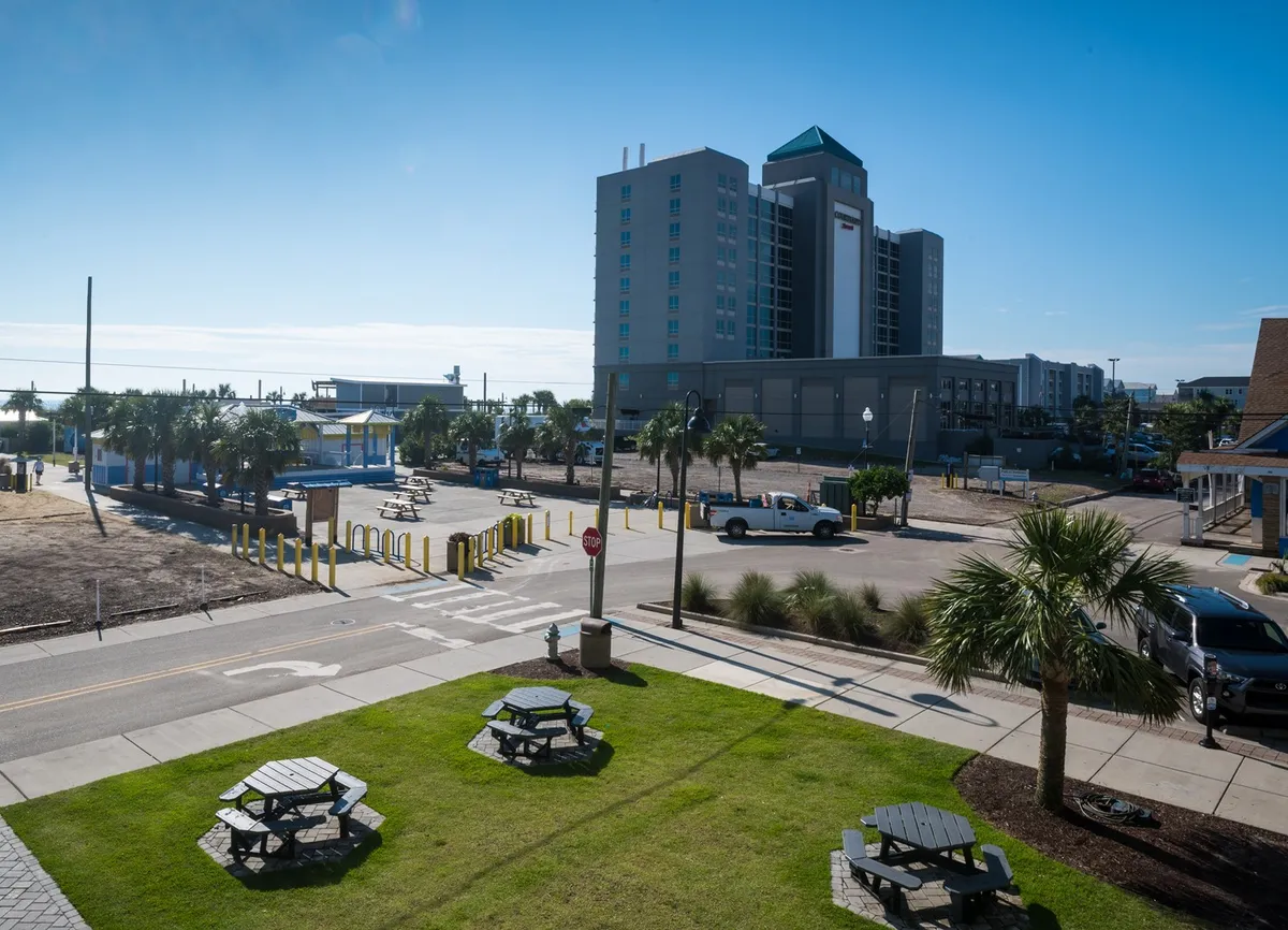 This exterior image showcases a tall building surrounded by palm trees and picnic tables, inviting visitors to enjoy sunny picnics and explore the nearby sights. The scene suggests proximity to recreational areas and highlights the relaxed, vacation-ready vibe of the property and its surroundings.