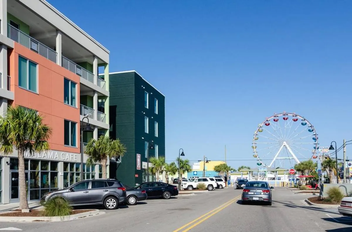 A cheerful scene featuring the Llama Cafe, colorful buildings, and a ferris wheel in the background. Couples can be imagined sharing a coffee, dining at the cafe, or enjoying the amusement park atmosphere, all set within a lively street environment.