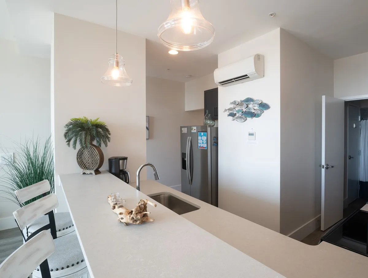 A cozy kitchen view focusing on the countertop, pendant lighting, decorative fish art on the wall, and a green plant. The scene feels inviting and relaxed, ideal for both casual breakfasts and festive dinners.